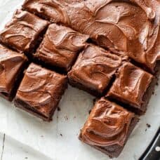 Overhead of a chocolate sheet cake cut into squares with one piece removed