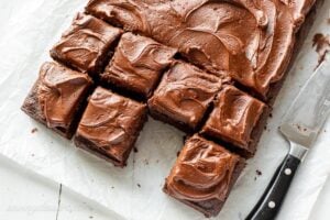 Overhead of a chocolate sheet cake cut into squares with one piece removed