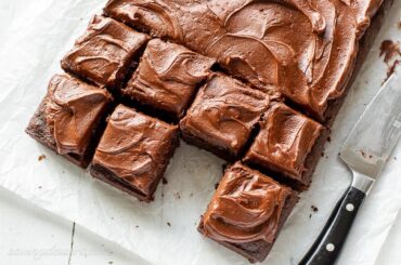 Overhead of a chocolate sheet cake cut into squares with one piece removed