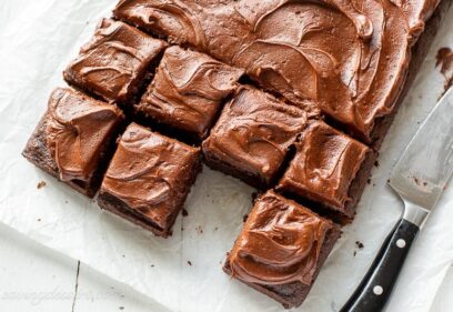 Overhead of a chocolate sheet cake cut into squares with one piece removed