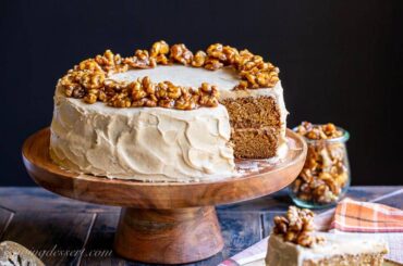 A side view of a sliced applesauce spice cake topped with brown sugar frosting and candied walnuts