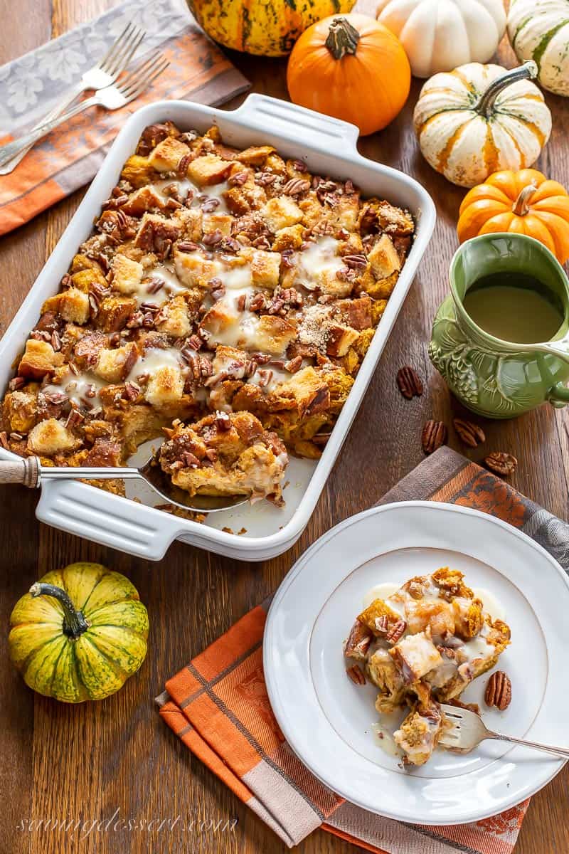 A table set with a casserole dish filled with pumpkin bread pudding and a slice on a plate with pumpkins around for decoration