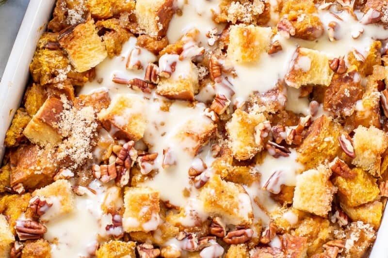An overhead view of a casserole dish filled with pumpkin bread pudding with a drizzle of bourbon sauce on top.