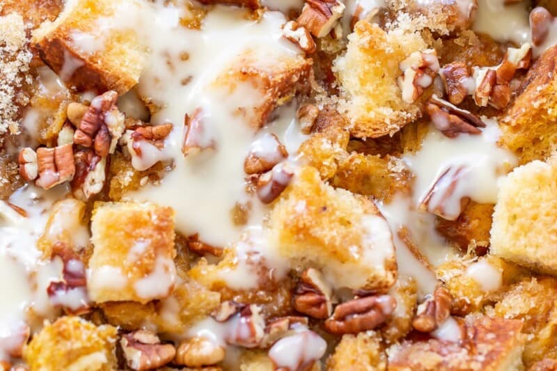 A closeup of a pan of pumpkin bread pudding drizzled with bourbon sauce and chopped pecans.