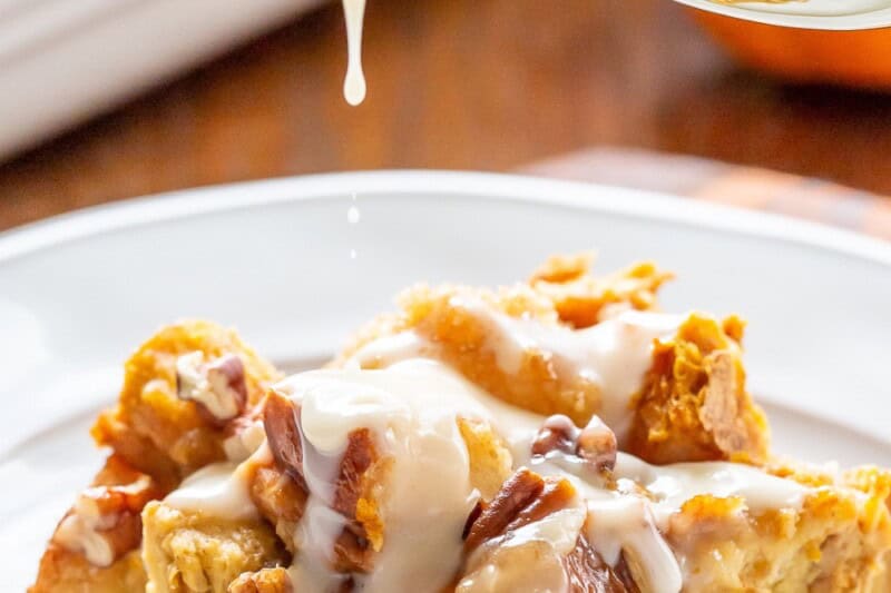 A pice of pumpkin bread pudding being drizzled with bourbon sauce.