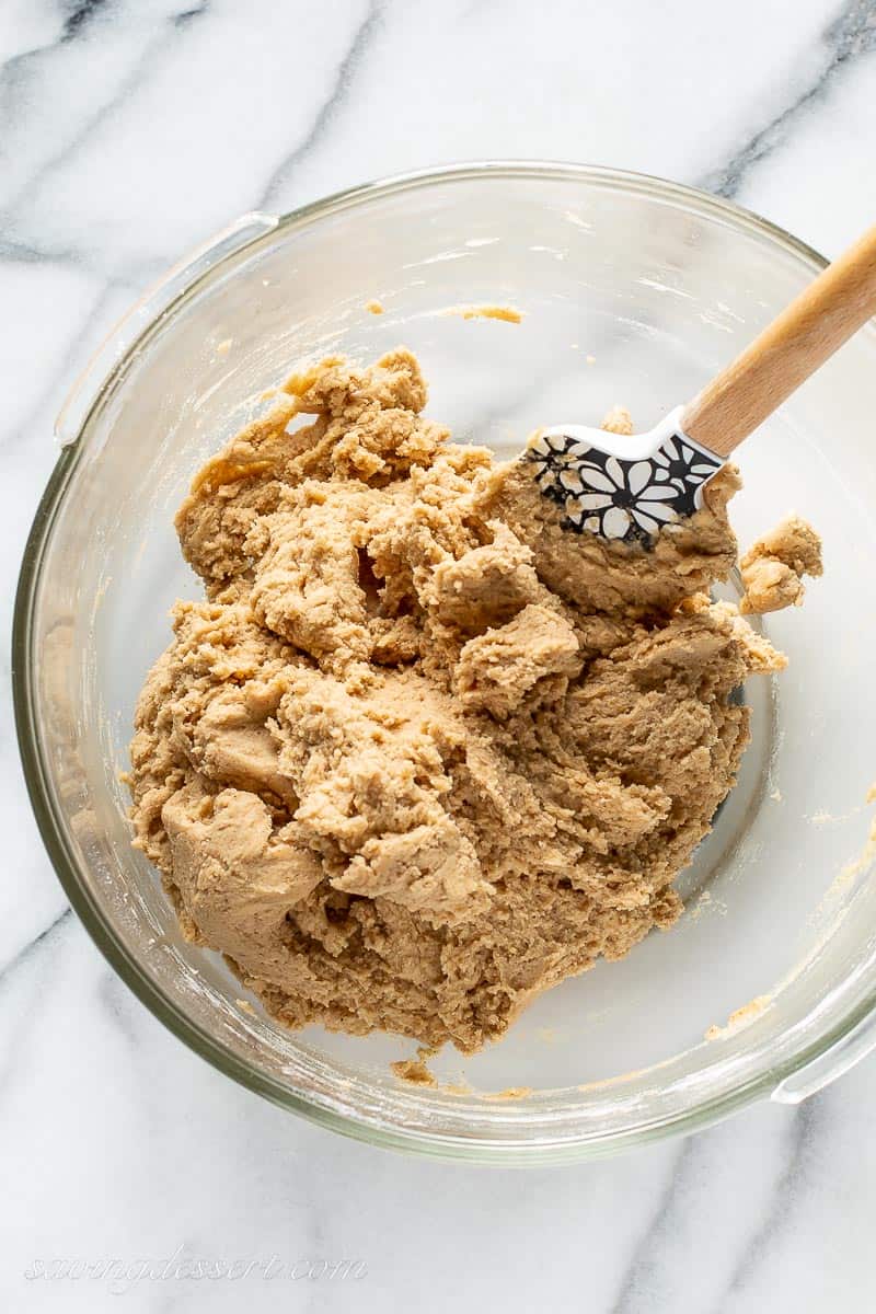 An overhead view of a mixing bowl with cookie dough and a spatula