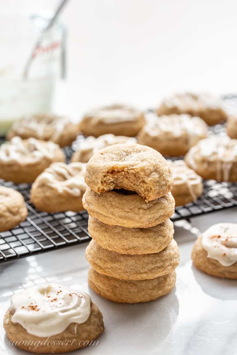 A stack of thick pumpkin spice cookies in front of a cooling rack filled with iced pumpkin spice cookies