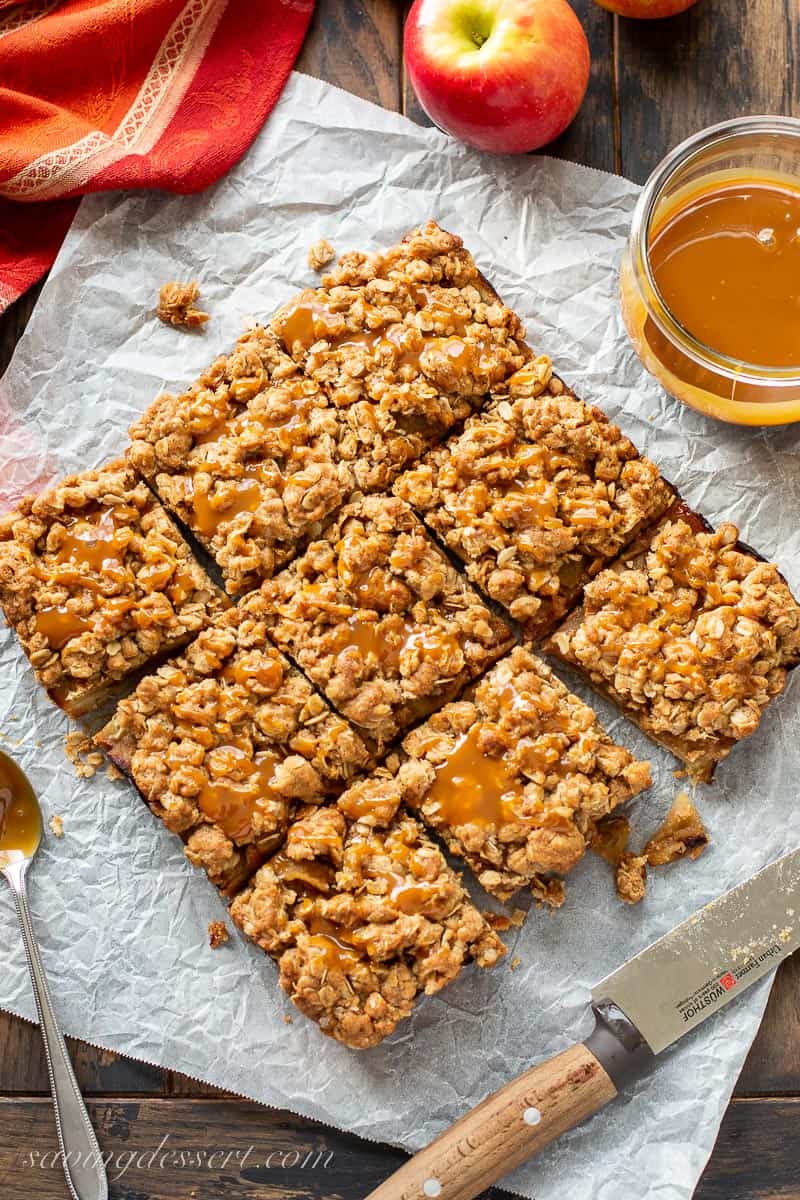 overhead view of a pan of sliced apple bars with apples and a jar of caramel in the background