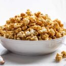 A side view of a big overflowing bowl of caramel popcorn