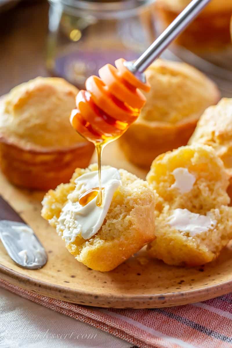 A plate of corn muffins with one split open with butter and honey