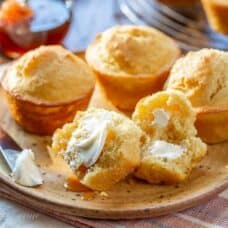 A plate with corn muffins with one split open topped with butter and honey