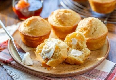 A plate with corn muffins with one split open topped with butter and honey