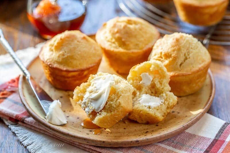A plate with corn muffins with one split open topped with butter and honey