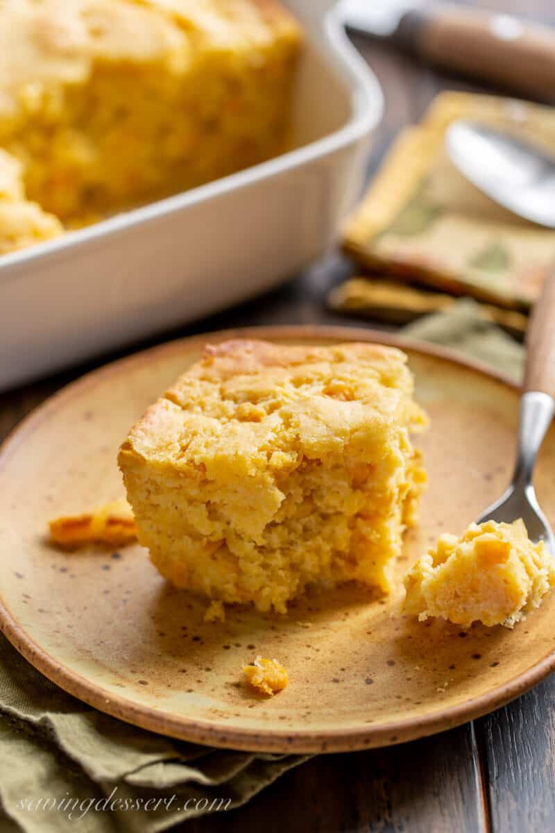 a square piece of corn pudding on a plate with a fork