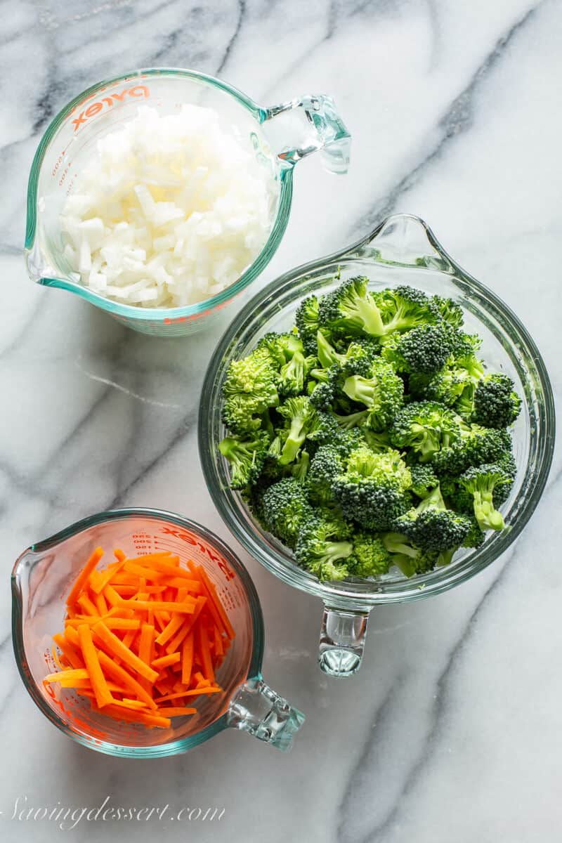 an overhead view of three bowls one with onions, broccoli and carrots