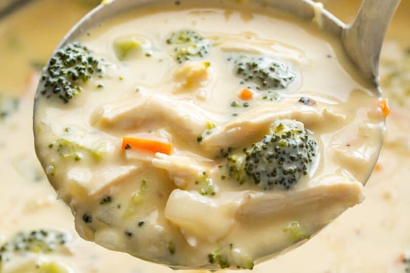 A pot of creamy broccoli soup with a ladle scooping soup out