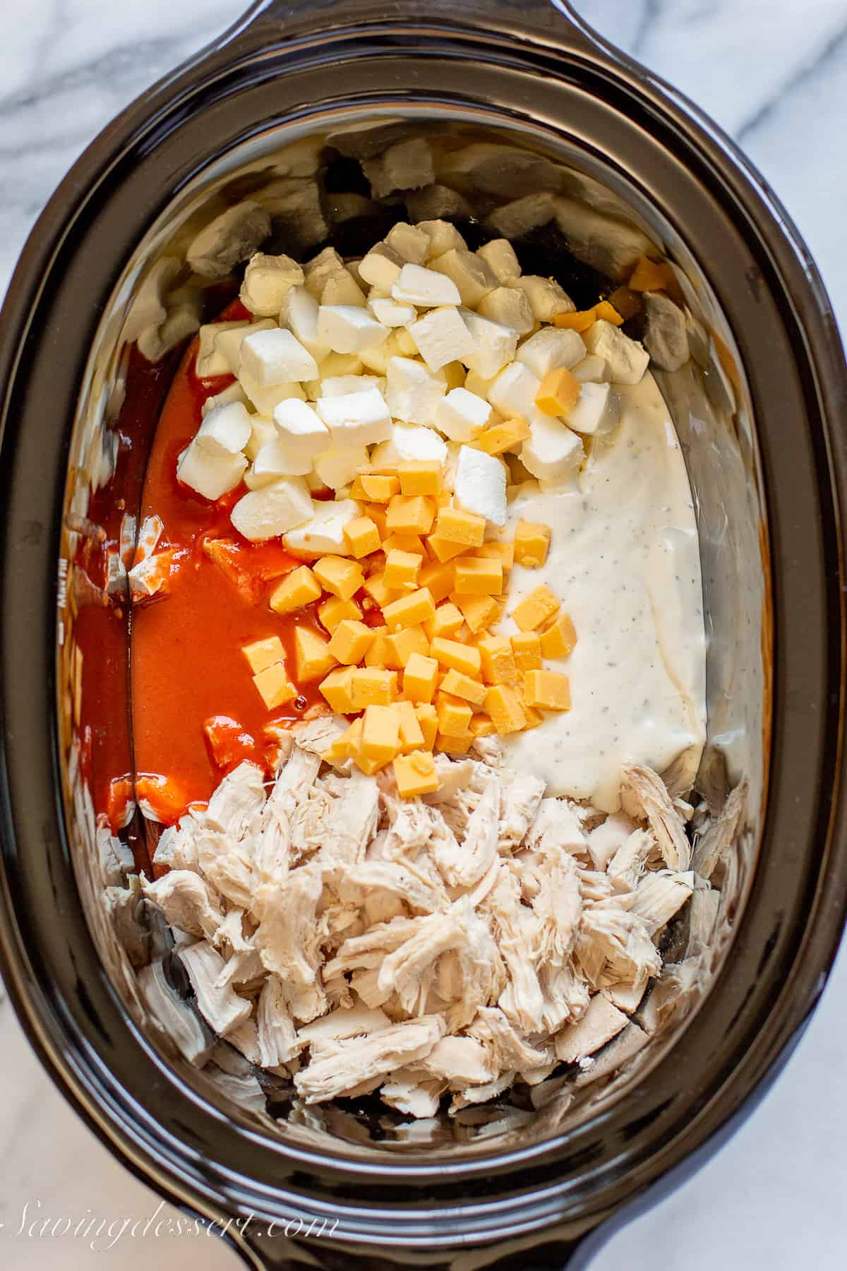 overhead view of a slow cooker filled with chicken, cheese, hot sauce, ranch dressing