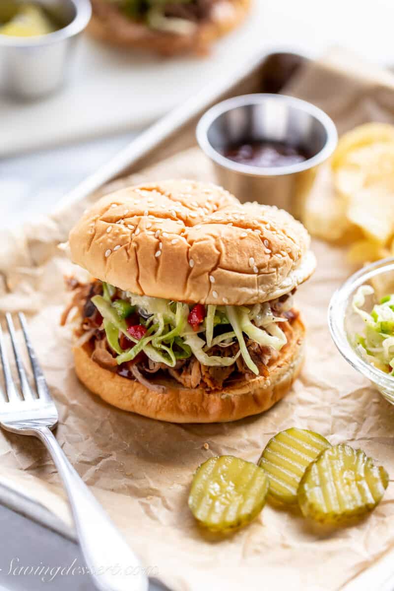 slow cooker pulled pork sandwiches on a tray with slaw, chips and pickles