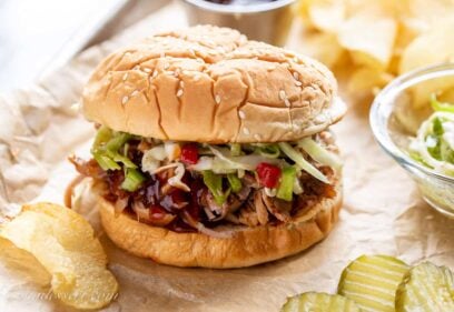 A pulled pork sandwich on a tray with chips, slaw and pickles