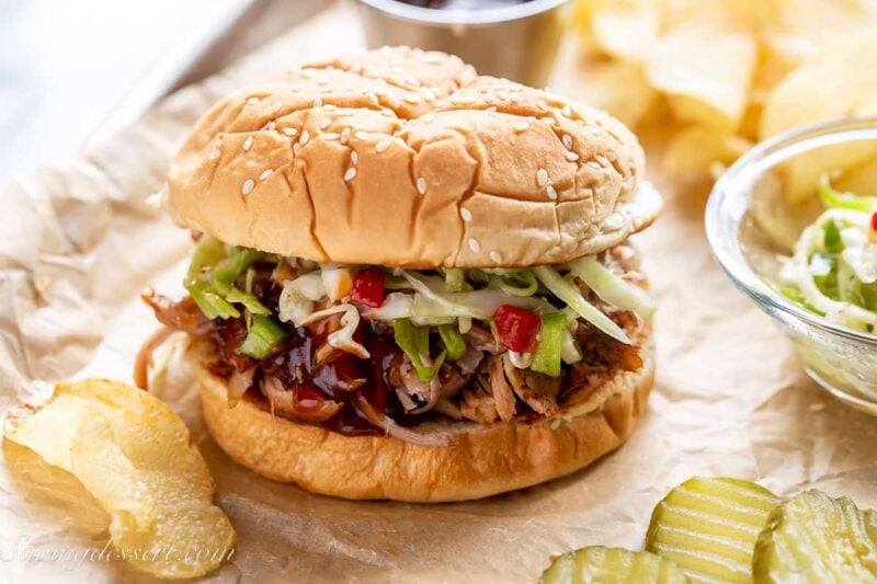 A pulled pork sandwich on a tray with chips, slaw and pickles