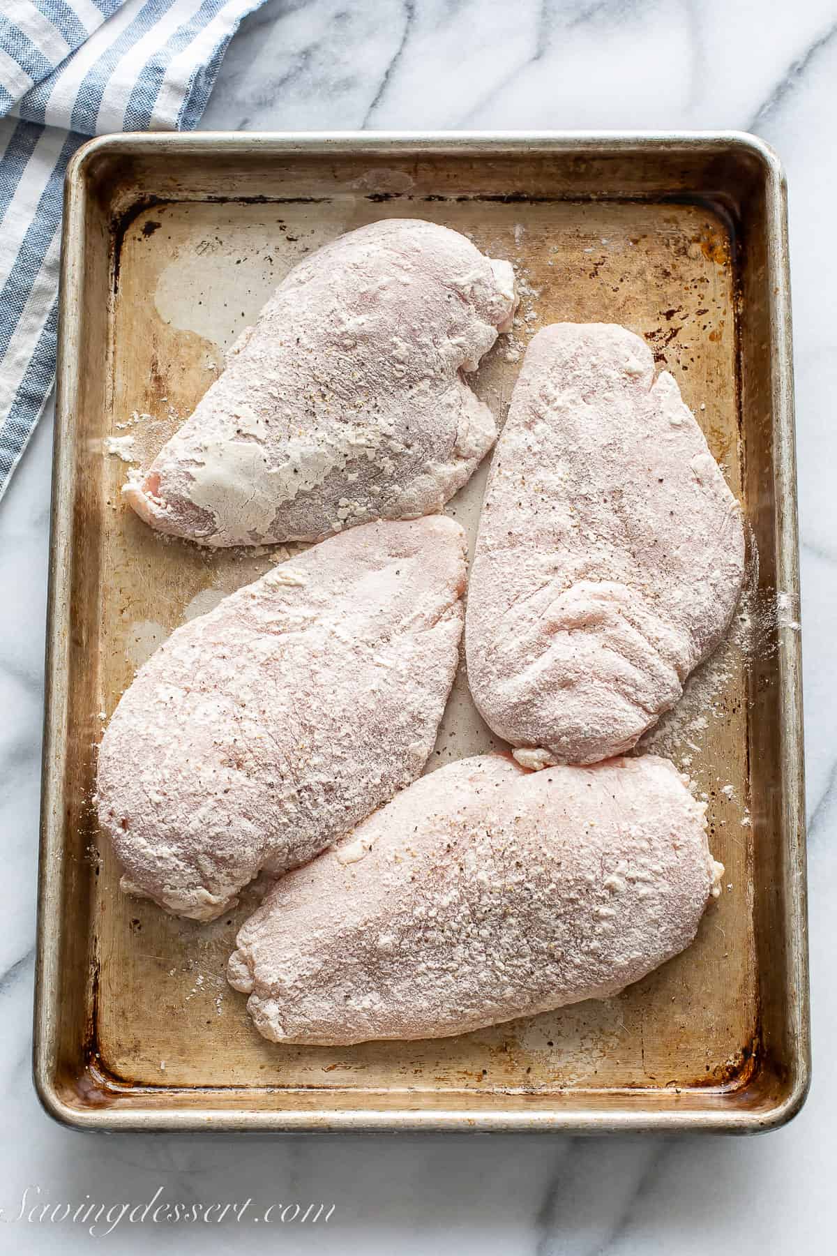 uncooked chicken breasts coated in flour on a baking tray
