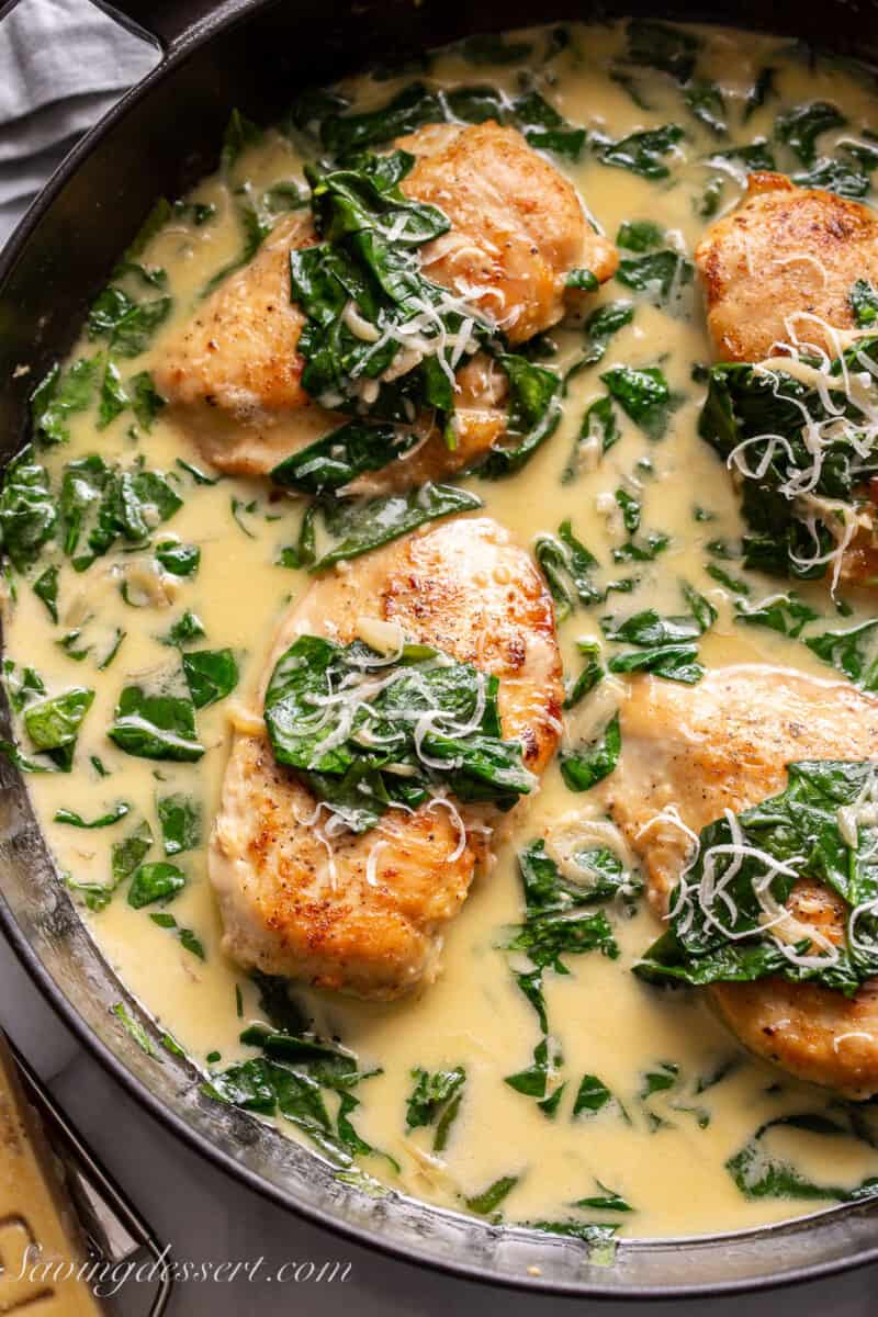 closeup of a skillet filled with chicken breasts and spinach in a cream sauce
