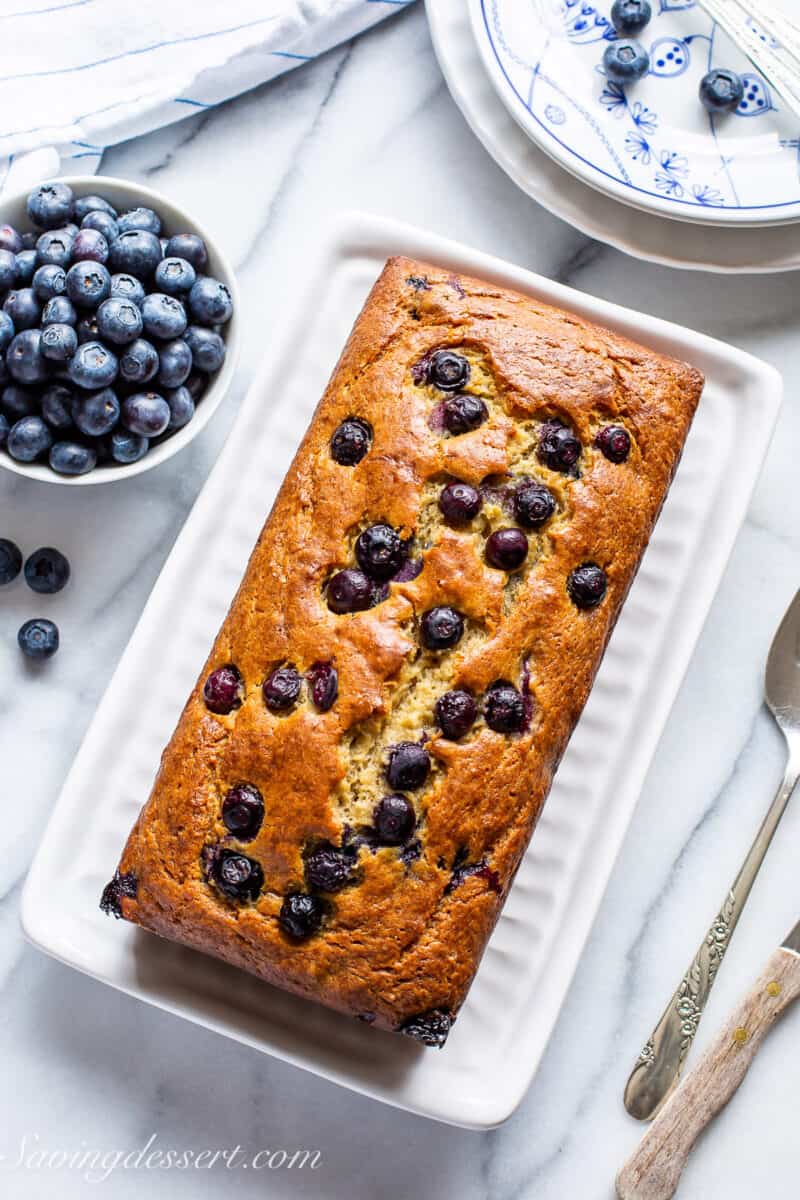 Overhead view of a loaf of blueberry banana bread on a table with blueberries on the side