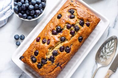 Overhead view of a fresh baked loaf of blueberry banana bread with blueberries and a spatula on the side