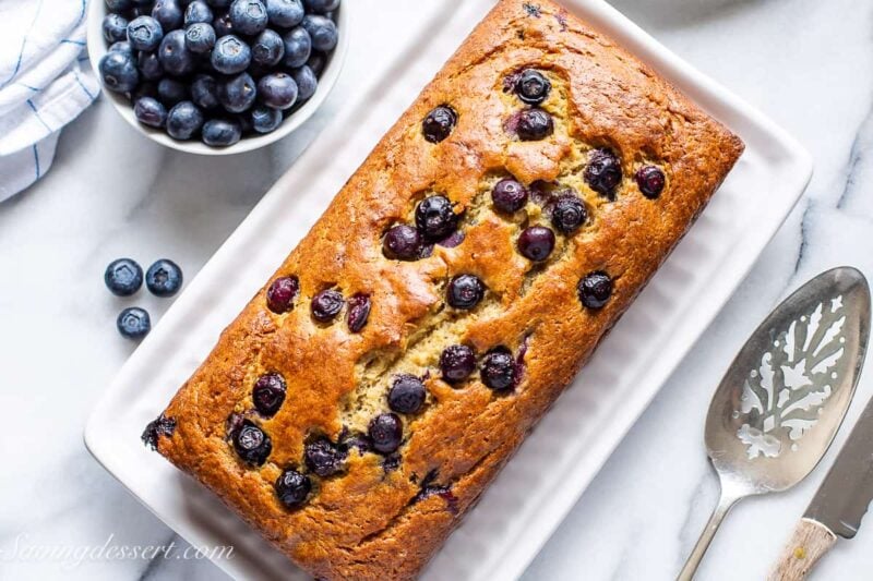 Overhead view of a fresh baked loaf of blueberry banana bread with blueberries and a spatula on the side