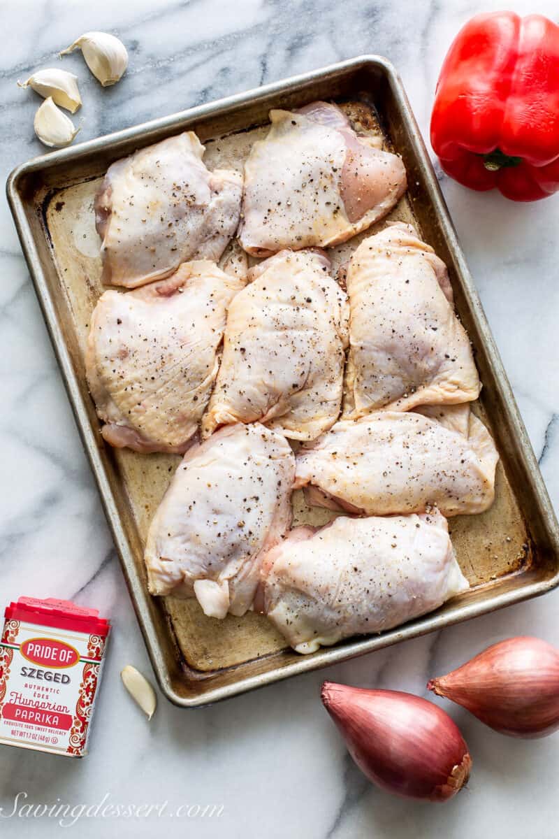 chicken thighs on a baking tray with a bell pepper, shallots, garlic and paprika