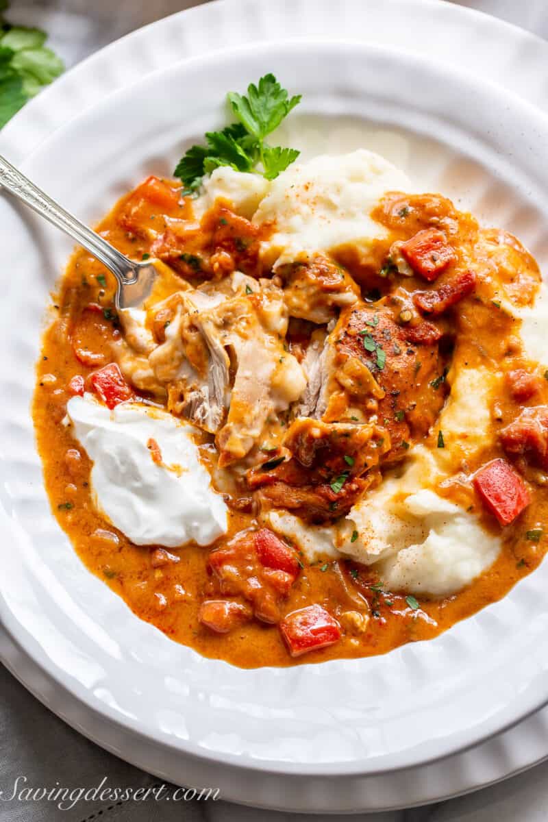 A bowl of mashed potatoes topped with a piece of chicken paprikash cut into pieces