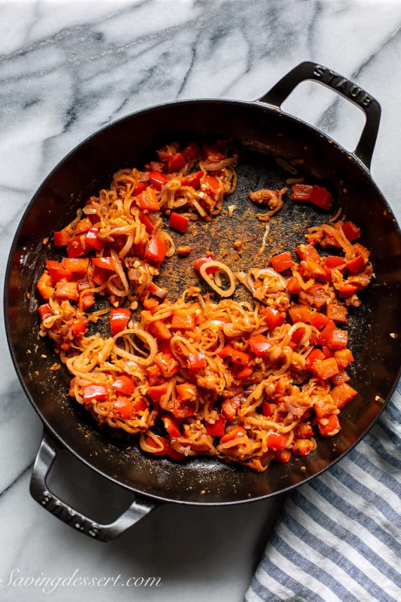 a skillet with red bell pepper, shallots and garlic with flour creating a fond on the bottom of the pan