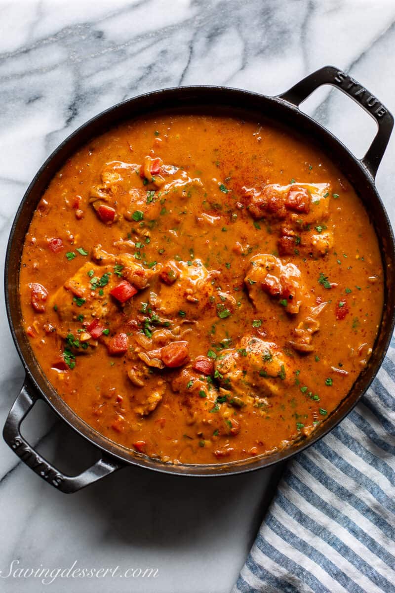 a skillet filled with a deep red sauce with chicken thighs