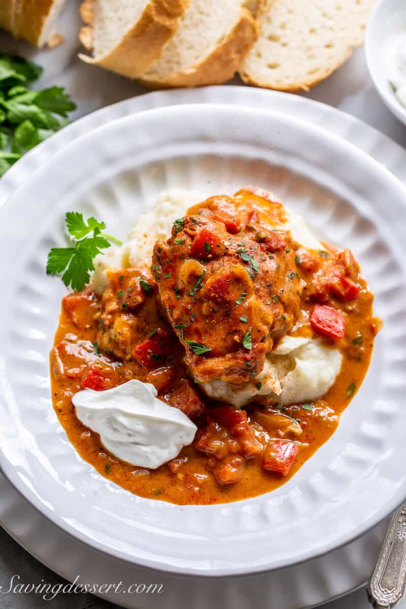 a wide bowl filled with mashed potatoes topped with a chicken thigh and chicken paprikash sauce