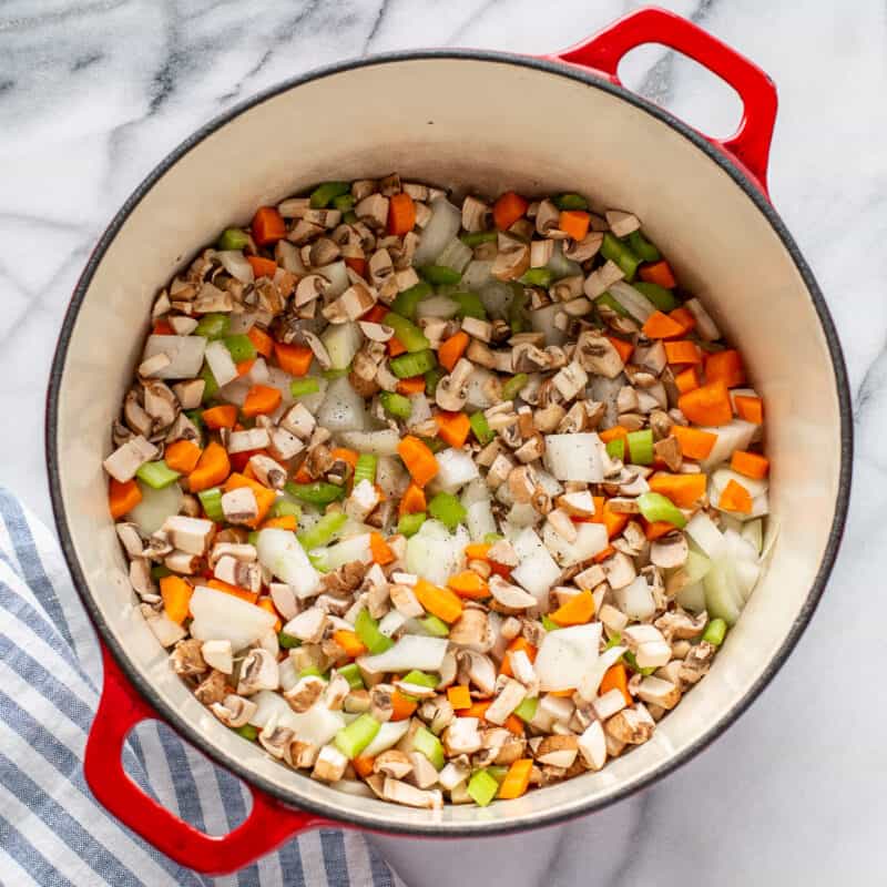 a Dutch oven filled with diced onion, carrot, celery and mushrooms