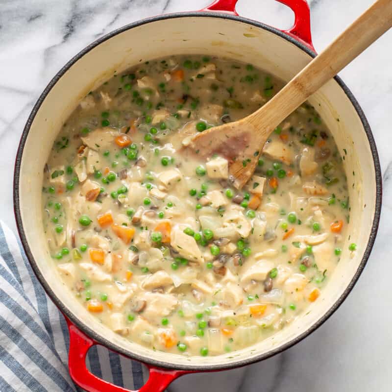 a Dutch oven filled with pot pie filling with peas, carrots and chicken