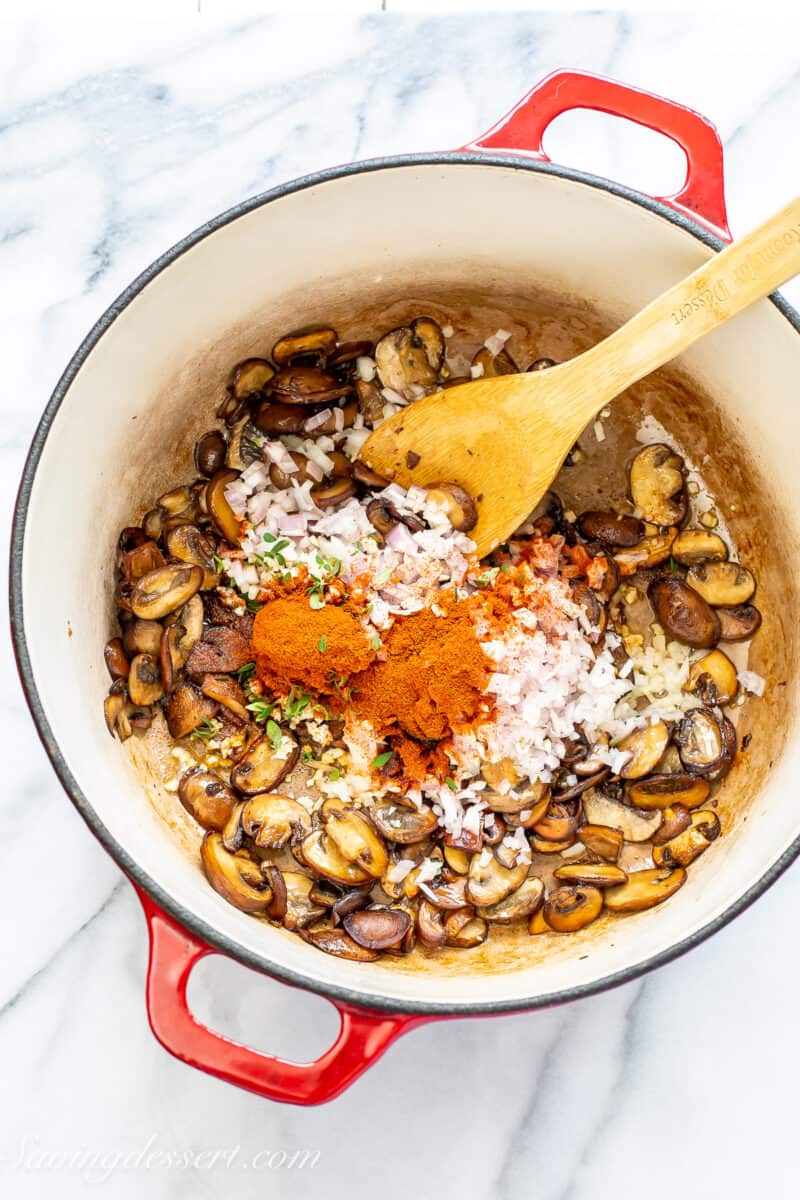 A Dutch oven with mushrooms, shallots, thyme leaves, garlic, tomato paste and paprika