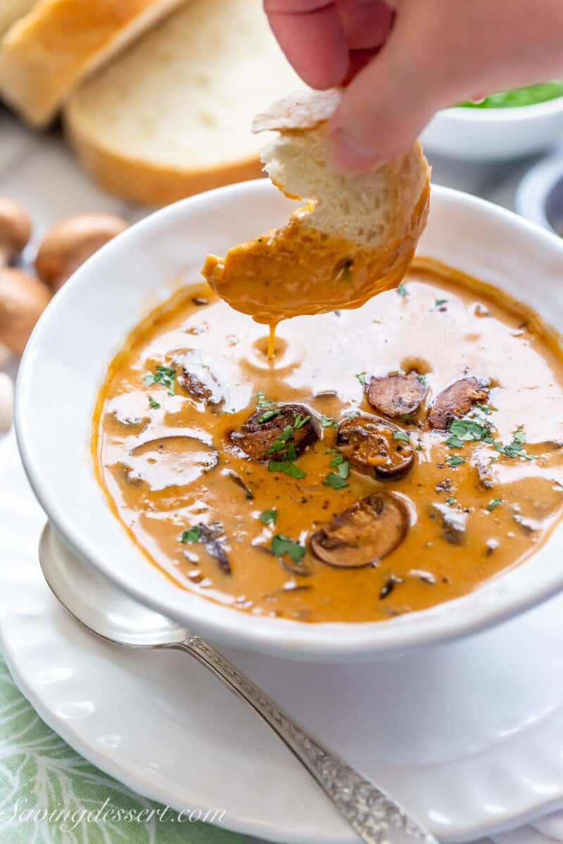 A piece of bread being dipped into a bowl of Hungarian Mushroom Soup