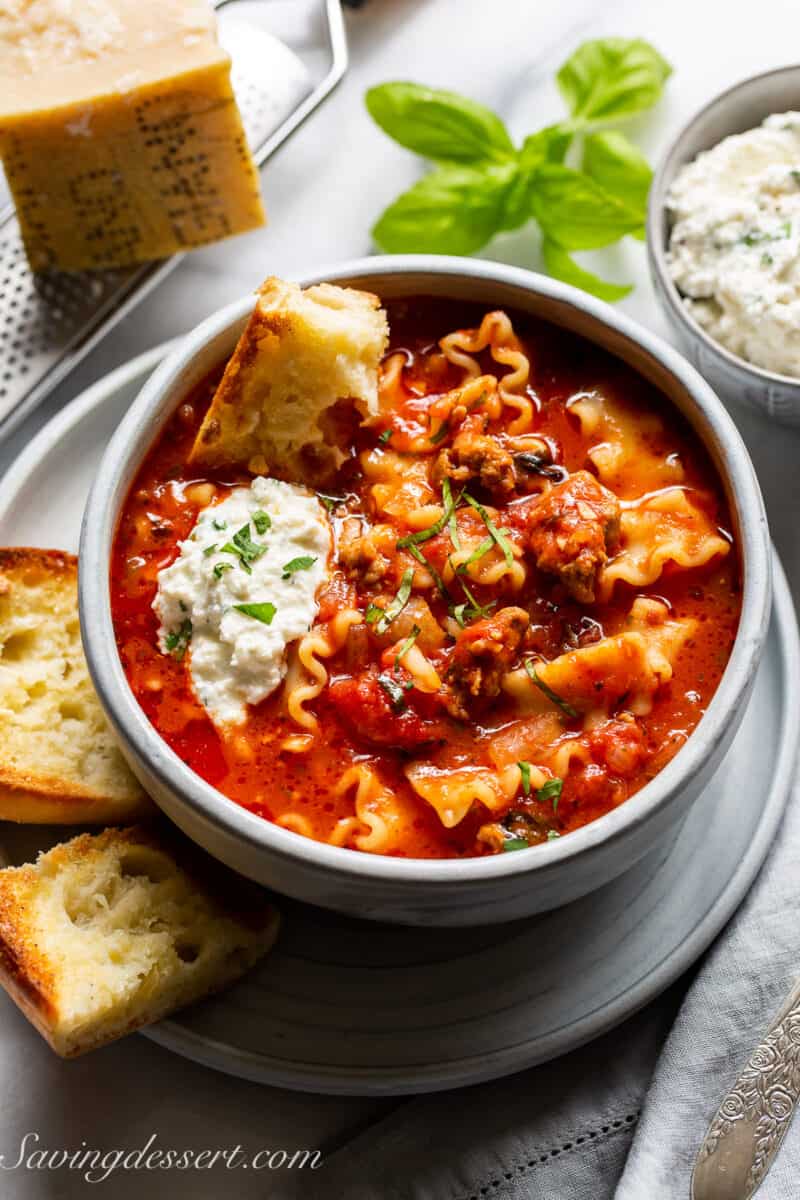 Lasagna Soup in a bowl with a dollop of ricotta cheese and a hunk of garlic bread