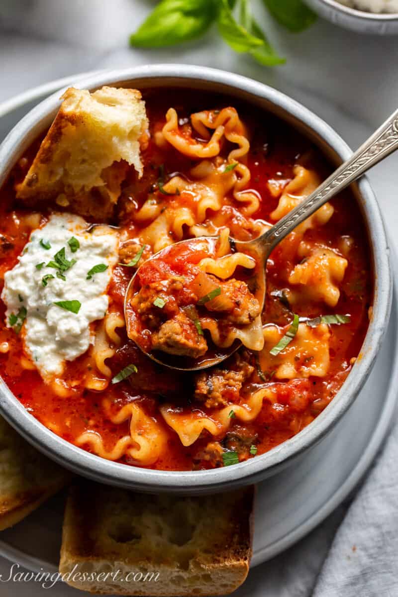 overhead view of a bowl of lasagna soup with ricotta cheese and a hunk of bread