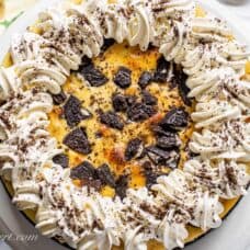 closeup of an oreo cheesecake decorated with whipped cream and oreo crumbs