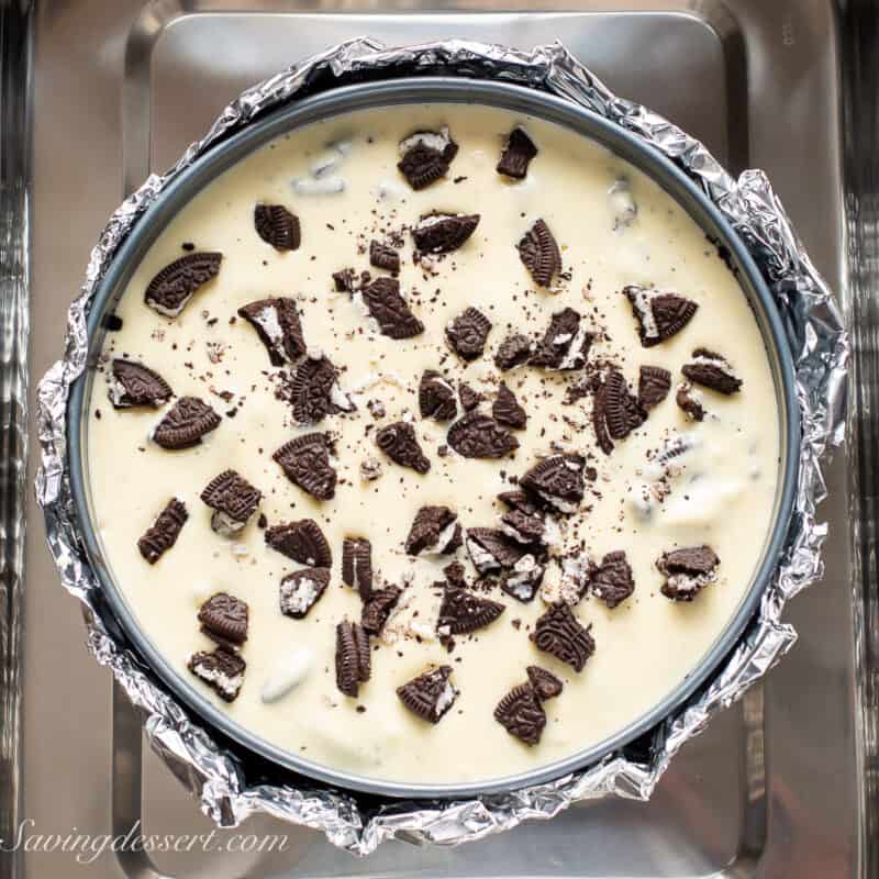 An unbaked oreo cheesecake in a hot water bath topped with chopped oreos