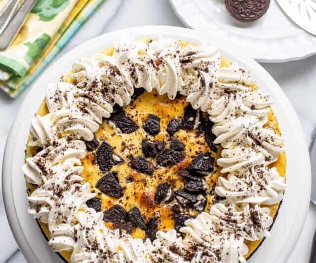 overhead view of an oreo cheesecake decorated with whipped cream and cookie crumbs on a cake platter