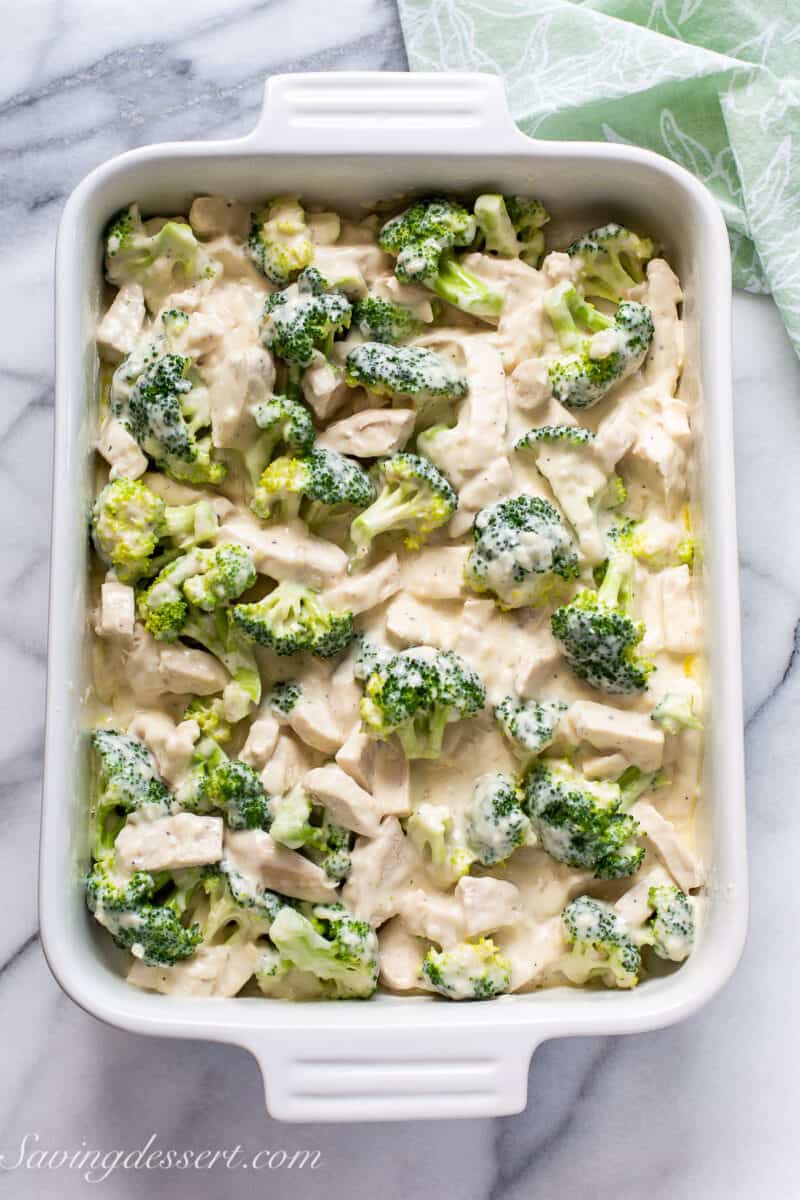 a casserole dish filled with unbaked broccoli and chicken in a creamy white sauce