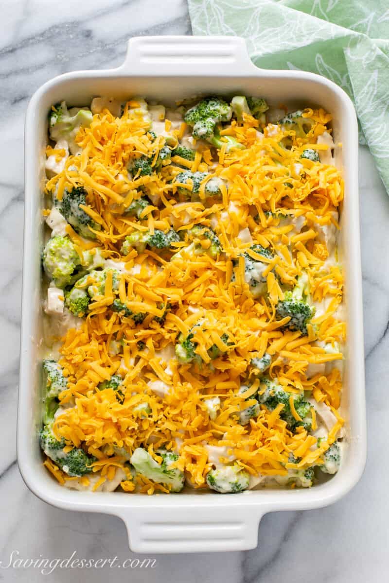 A unbaked chicken casserole topped with shredded cheddar cheese