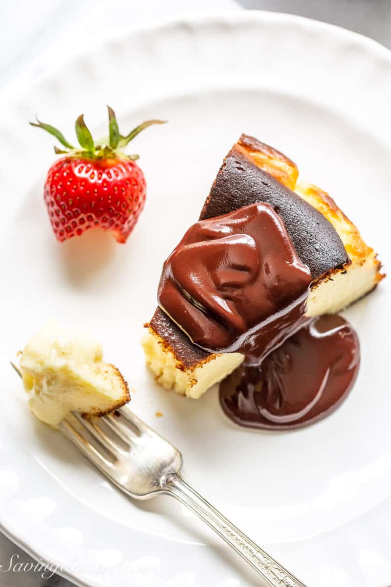 overhead view of a piece of basque cheesecake on a plate topped with silky chocolate sauce and strawberries