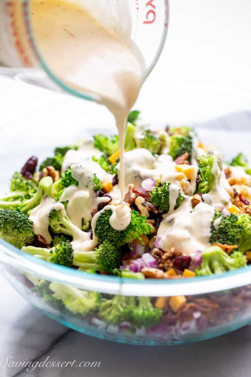 a bowl of broccoli salad being drizzled with a creamy white dressing