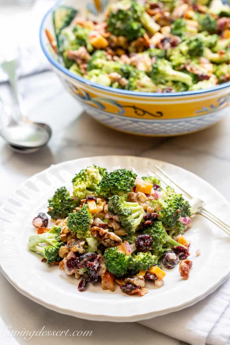 a plate of broccoli salad with a bowl of the same salad in the background