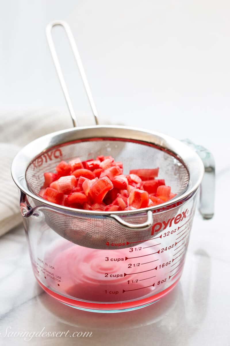 a fine mesh strainer filled with sliced rhubarb set over a measuring cup.
