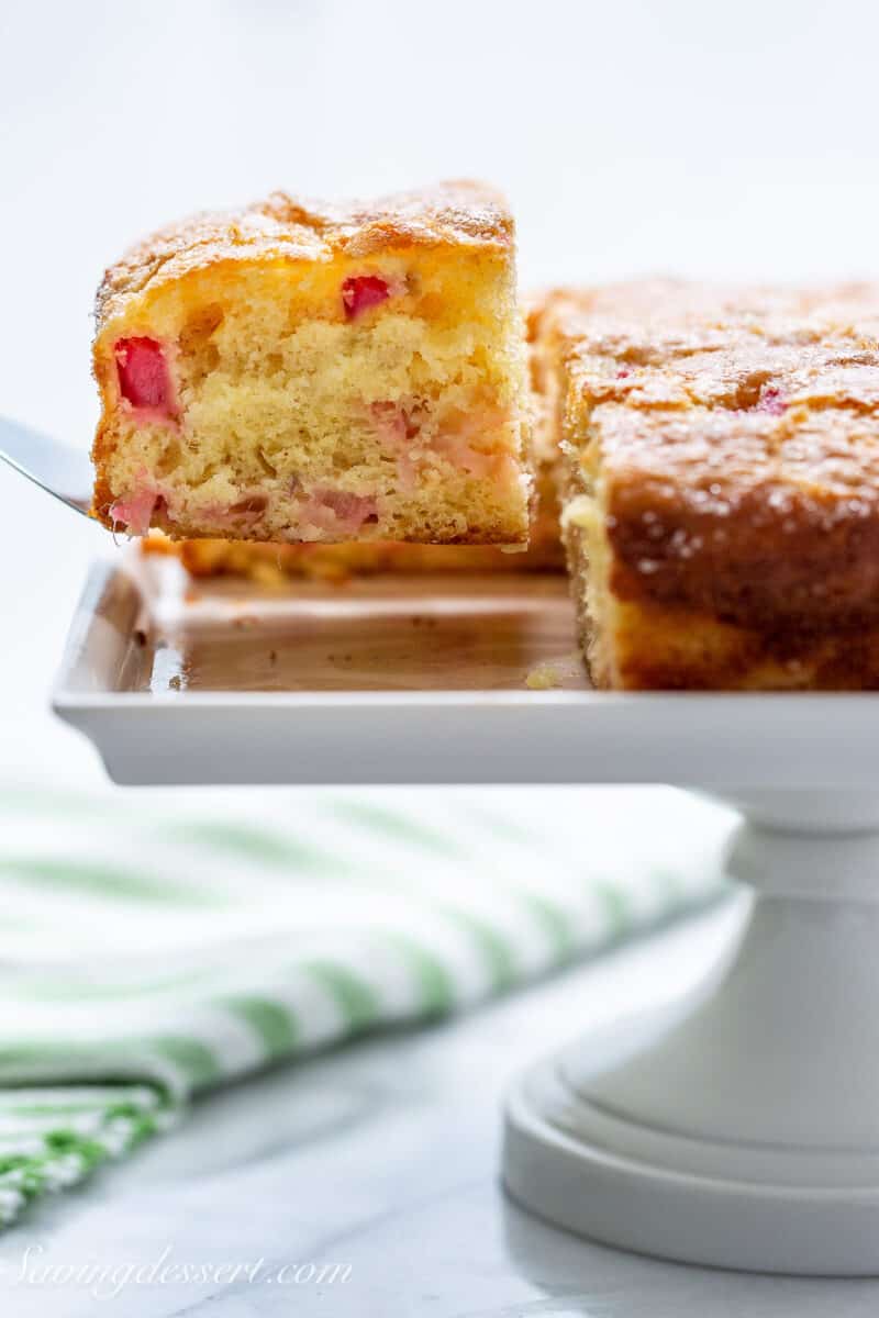 a side view of a rhubarb cake on a cake stand with a slice on a spatula